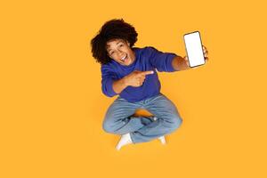 A guy is seated on the floor, his finger extended to point at a cell phone with white screen in his hand. He seems to be engaged with the device, possibly showing something on the screen. photo