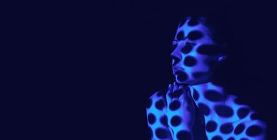 The image shows a womans face and upper body illuminated by blue light. The light creates a pattern of dots on her skin, like a pointillist painting. Her hands clasped in front of her, copy space photo
