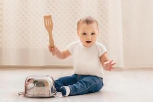 A small baby is seated on the floor, gripping a spatula in their tiny hands. The infant seems curious and engaged as they explore the kitchen utensil. photo