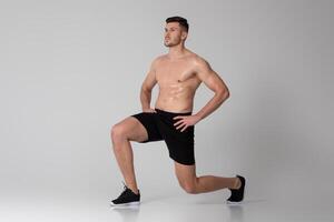 A man is exercising by performing squats on a gray background. He is bending his knees and lowering his hips, then pushing back up to a standing position photo