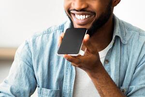 A man speaks into his phone, using a voice assistant. He is smiling and appears to be enjoying the experience. photo