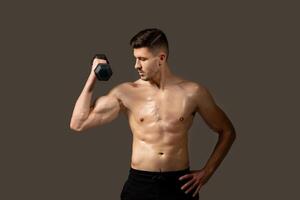 A shirtless man is seen holding a dumbbell in a gym setting. He appears focused and engaged in his workout routine, displaying strength and determination. photo