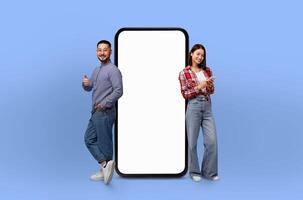 Asian couple standing next to a large-sized telephone, looking at the device with curiosity. The phone appears oversized in comparison to the people, creating a unique visual contrast. photo