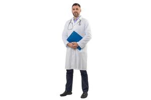 A man doctor is standing with a blue folder in his hands while wearing a white lab coat. He looks composed and professional, implying readiness for medical consultations. photo