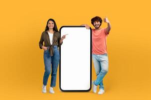 Indian man and woman are standing together, pointing at a blank screen of a phone. They appear focused and engaged, possibly discussing content or demonstrating a feature on the device. photo