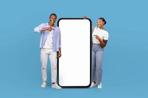 African American couple stand, a smile on each of their faces, next to a large smartphone that features a blank screen, providing a versatile backdrop for creative projects. photo