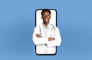 A black man doctor is attentively looking at his phone screen with a stethoscope attached, possibly checking medical information or communicating with colleagues. photo