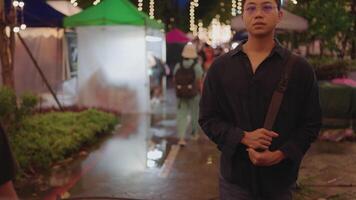 A man wearing glasses and a shoulder bag walks through a lively night market with lights. He feels depressed, unemployed, and failed a job interview. A charming and depressed young man feels uneasy video