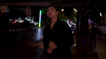 retrato de hermoso grave joven hombre esperando para un autobús en el lluvia, noche ciudad con bokeh neón luces en el antecedentes. tristeza, depresión, despedido. confidente y enfocado joven hombre pensamiento. video