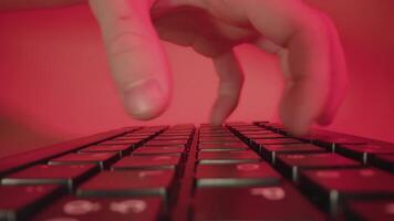 Person types fast on keyboard working at table on red video