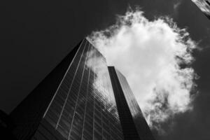 Black and white photograph of a tall building with a cloud in the sky photo