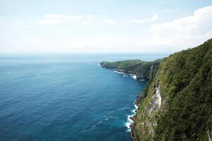 Landscape of wave crashing rocky cliff and wild on stone mountain at the blue calm sea with sponge on summer with ocean for destination in Bali island at Indonesia photo