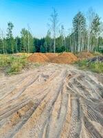 Landscape view of a dirt construction site with piles of soil and visible tire tracks, against of a forest . High quality photo