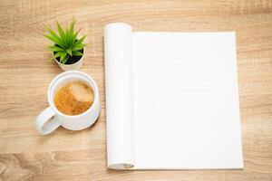 Glass of hot coffee with an open empty magazine on a wooden table or desk from above in mock up concept. photo
