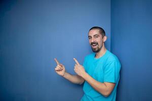 Young man pointing empty space using hands and fingers, isolated over blue background photo