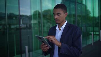 A businessman is effectively using a tablet while standing outside a modern glass building video
