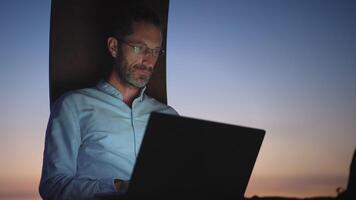 uma focado profissional acionado dentro trabalhos às crepúsculo enquanto usando uma computador portátil para pegue coisas feito video