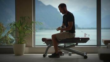 A man is diligently working out with dumbbells next to a large window, enjoying the view video