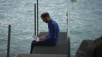 A person is diligently working on their laptop while sitting comfortably by the waters edge video