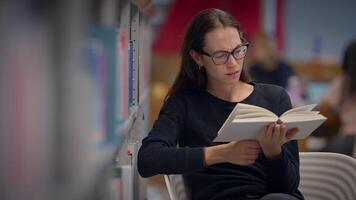 A young woman is deeply engaged in reading a book within a cozy library setting filled with books video