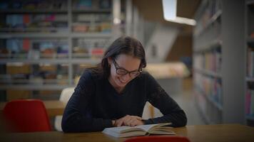 un joven mujer es disfrutando un cautivador libro en un moderno biblioteca, lleno de concentración video