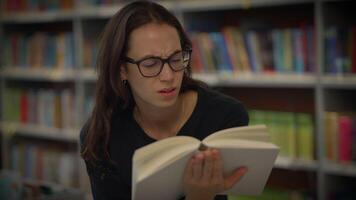 A Focused Woman Sitting Quietly and Reading in a Library Surrounded by Books and Knowledge video