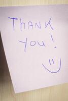A sticky note hanging on the wall, with the text Thank You on it. photo