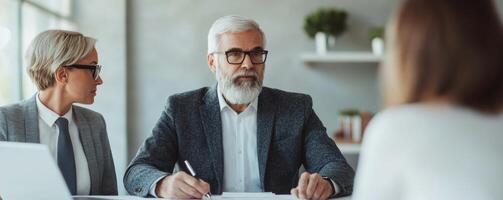 A senior businessman with a beard engages in a professional meeting, flanked by two colleagues, discussing strategies with focused expressions in a modern workspace. photo