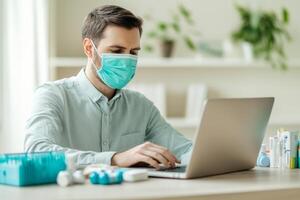 Young man in a mask working on a laptop at home with a tidy workspace and office supplies. photo