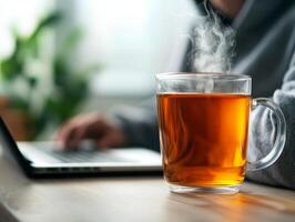 A steaming cup of tea on a desk near a laptop, creating a cozy workspace atmosphere. photo