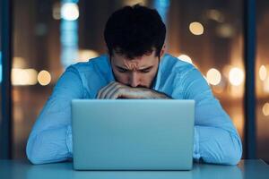 Frustrated man working at laptop in a dimly lit office environment. photo