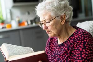 Elderly woman reading a book indoors, focused and engaged in the moment. photo