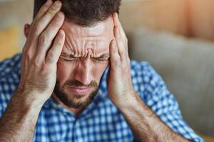 Frustrated man with headache, hands on head, stressed expression, blurred background. photo