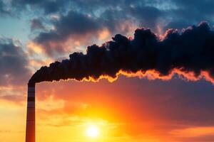 Pollution from smoke stack against a vibrant sunset and clouded sky. photo