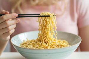 Person holding chopsticks with noodles in a bowl, soft background. photo