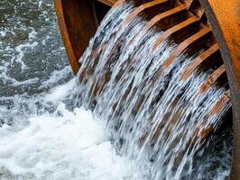 Water flow from a rustic water wheel, creating ripples in the stream. photo