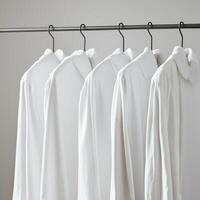 Four hanging white shirts on a rack against a minimalist background. photo