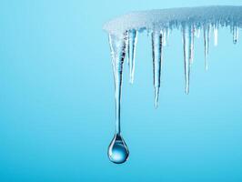 Icicles hanging from a roof against a blue background, water droplet forming beneath. photo
