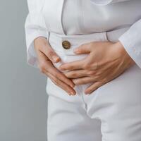 Person in white outfit holding stomach, expressing discomfort or concern. photo