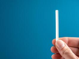 Hand holding a white stick against a blue background. photo