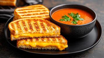 Grilled cheese sandwiches with tomato soup in a black bowl on a dark table. photo