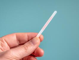 Hand holding a thermometer on a pastel background. photo