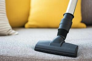 Vacuum cleaner on beige fabric sofa with yellow cushions. photo