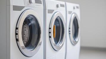 Three modern washing machines in a clean laundry room with grey tones. photo