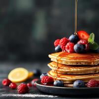 Stack of pancakes topped with berries and syrup on a dark background. photo