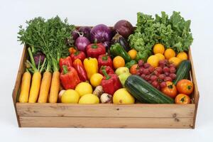 Colorful assortment of fresh vegetables and fruits in a wooden crate, white background. photo