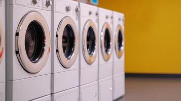 Row of modern washing machines against a vibrant yellow wall. photo