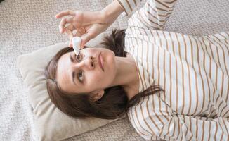 Top view of a woman who drips antibacterial drops into her eyes while lying on the couch photo