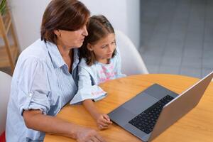 From above of granddaughter and grandmother using laptop on table photo