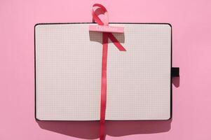 Open notebook on pink background with October tag and ribbon symbolizing planning and creativity photo